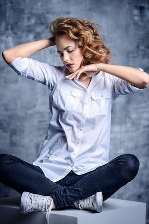 Fashion shot. Beautiful female model posing at studio in white shirt and black jeans. Youth style.の写真素材