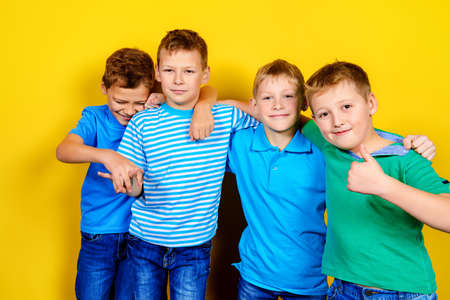 Four boys best friends standing together. Bright yellow background. Summer fashion.の写真素材
