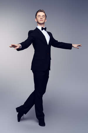 Elegant young man dancer in black suit and bow-tie posing at studio. Male ballet dancer.の写真素材