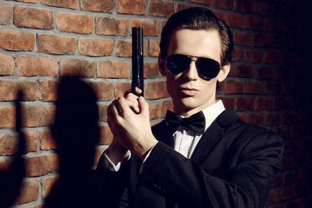 Handsome man in black suit and sunglasses holding a gun. Secret agent, mafia.