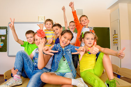 Group of happy classmates in bright casual clothes posing together at a classroom. Education.