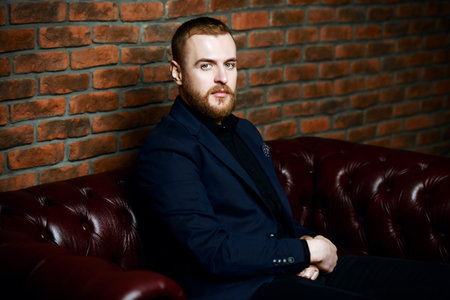 Imposing well dressed man sitting on a Chesterfield leather couch. Men's beauty, fashion.