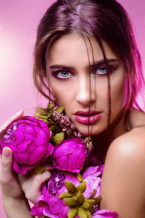 Beauty portrait. Gorgeous young woman with bright make-up posing with peony flowers. Perfumes and cosmetics. Fashion concept.の写真素材