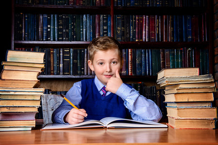 Smart boy in a suit sitting in the library by the bookshelves with many old books. Educational...