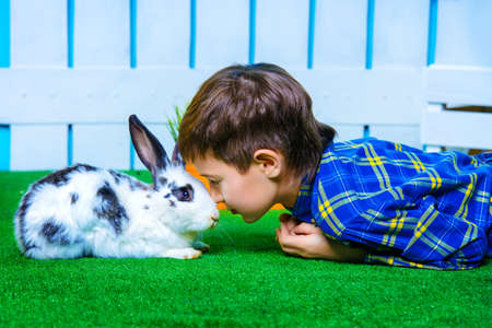 Happy child boy lying on a grass with Easter Bunny in spring garden decoration. Kid's fashion. Easter holidays.の写真素材