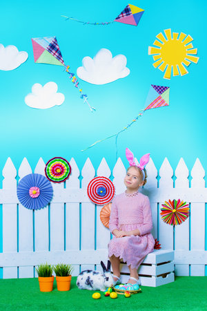 Cute happy little girl sitting with Easter Bunny in spring decorations. Easter Bunny and painted...