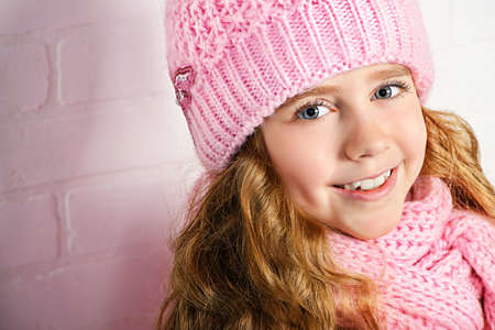 Winter clothes concept. Pretty smiling girl with long curly hair wearing pink knitted hat and scarf and smiling at camera.の写真素材