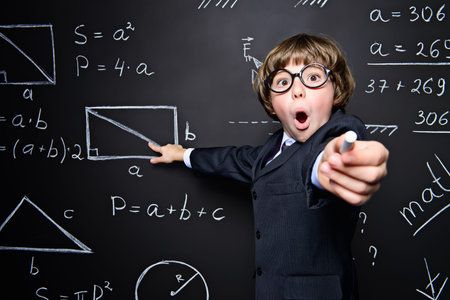 Smart schoolboy in black suit and glasses explaning something emotionally at the blackboard....