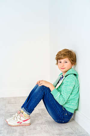 Pretty nine-year girl sitting on a floor leaning against the wall. Children's fashion. Education. Activity and child concept. Copy space.の写真素材