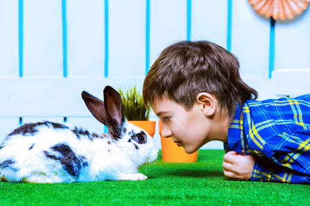 Happy child boy lying on a grass with Easter Bunny in spring garden decoration. Kid's fashion. Easter holidays.の写真素材