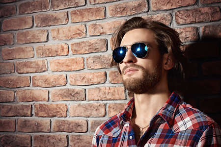 Handsome young man in sunglasses standing against the brick wall. Men's beauty, fashion. Men's barbershop, Hairstyle.の写真素材