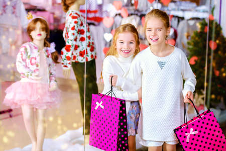 Two cute little girls standing near the shop window. Shopping concept. Kid's fashion. Modern children. Seasonal sale, shopping.の写真素材