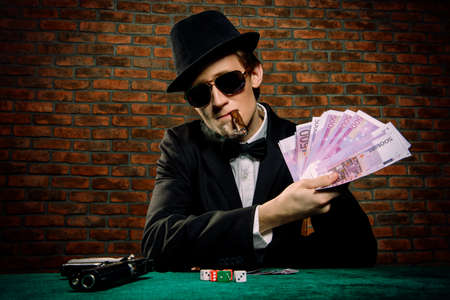 Cool mafia gangster with a gun sitting at a game table in a casino. Gambling, playing cards and roulette.の写真素材