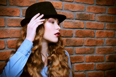 Close-up portrait of an attractive girl with long curly hair standing by the brick wall. Hipster girl. Youth fashion, beauty. Long hair, haircare.の写真素材