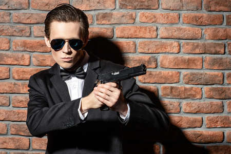 Handsome man in black suit and sunglasses holding a gun. Secret agent, mafia.の写真素材