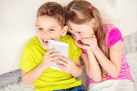 Two cheerful laughing children spending time at home with tablet pc.の写真素材