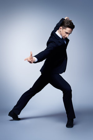 Elegant young man dancer in black suit and bow-tie posing at studio.