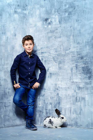 Kid's fashion. Modern nine year old boy posing with rabbit. Clothes for children. Easter holidays.の写真素材