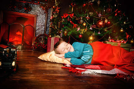 Christmas concept. Cute little boy fell asleep under the Christmas tree waiting for Santa Claus. Time for miracles.の写真素材
