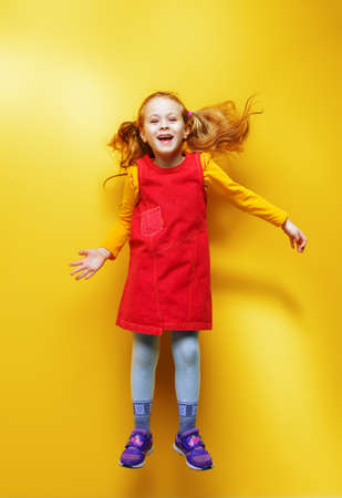 Happy five year old girl in bright summer clothes jumping for joy over yellow background. Happy childhood. Copy space.の写真素材