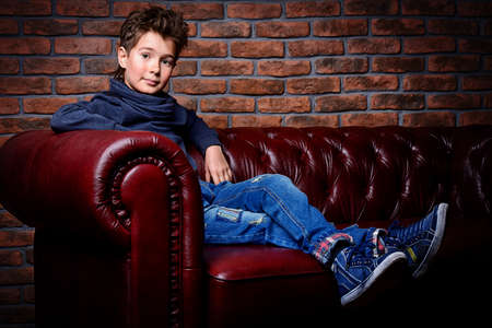 Kid's fashion. Modern nine year old boy posing at studio over brick wall background. Clothes for children.の写真素材