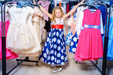 Pretty little girl child choosing a new dress in the shop of children's clothes. Seasonal sale and shopping. Kid's fashion.の写真素材