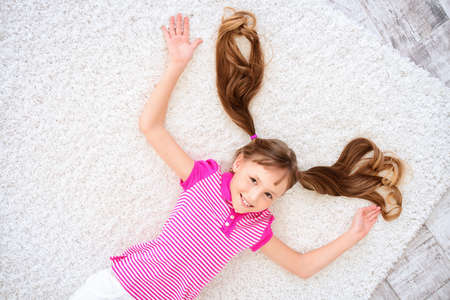 Joyful smiling child girl lying on a floor and having a rest at home. Happy childhood.の写真素材