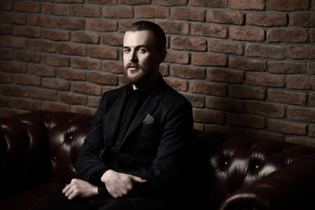 Imposing well dressed man sitting on a Chesterfield leather couch. Men's beauty, fashion.
