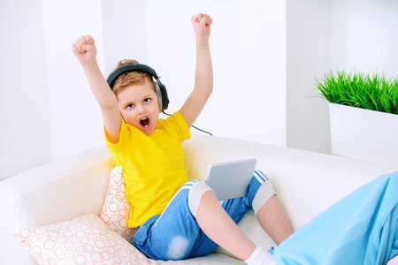 Joyful excited boy listening to music in headphones at home. Happy childhood. Activity for children.