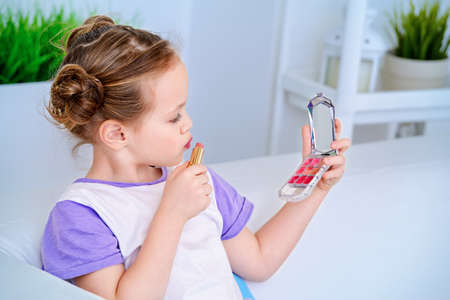 Cute little girl paints lips with mom's lipstick. Beauty, kid's fashion.の写真素材