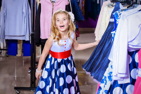 Pretty little girl child choosing a new dress in the shop of children's clothes. Seasonal sale and shopping. Kid's fashion.の写真素材