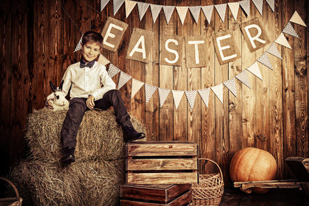 Easter holidays. Happy child boy sitting on a haystack with Easter Bunny.