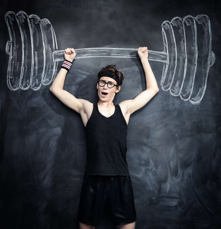 Funny skinny guy raises huge heavy barbell, drawn on a blackboard. Sports and health concept.の写真素材