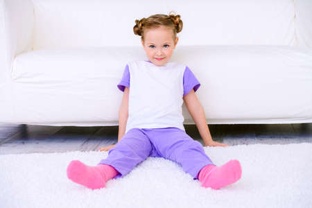 Cute little girl sitting on a carpet at home. Leisure. Family at home.の写真素材