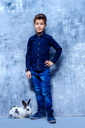 Kid's fashion. Modern nine year old boy posing with rabbit. Clothes for children. Easter holidays.の写真素材