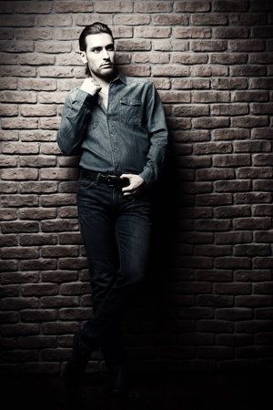Jeans style. Full length portrait of a handsome young man in jeans clohes standing against the brick wall. Men's beauty, fashion. Men's barbershop, Hairstyle.の写真素材