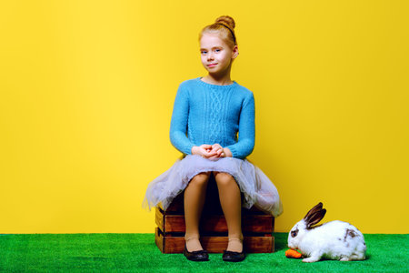 Cute smiling child girl sitting on a grass with Easter bunny and painted eggs. Easter holidays....