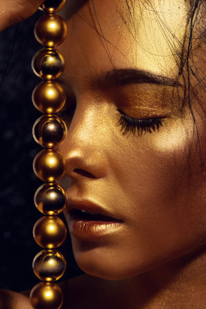 Beauty concept. Close-up portrait of a beautiful young woman with glowing golden skin. Skin care products, cosmetics. Jewellery concept.の写真素材