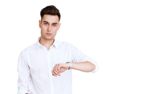 Portrait of a handsome young man in white shirt looking at the wristwatch. Men's beauty, fashion. Businessman. Copy space.の写真素材