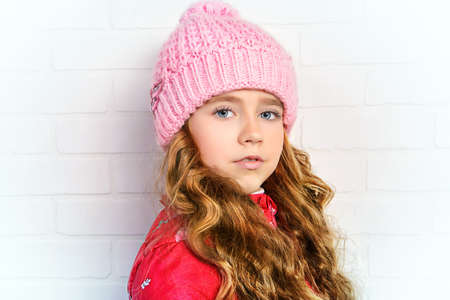 Winter clothes concept. Pretty smiling girl with long curly hair wearing pink knitted hat and smiling at camera.の写真素材
