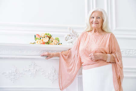 Modern well-groomed old woman with beautiful blonde hair standing in a room with a classic interior. Beauty, fashion. Luxury.の写真素材