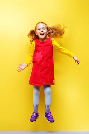 Happy five year old girl in bright summer clothes jumping for joy over yellow background. Happy childhood. Copy space.の写真素材