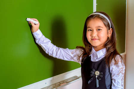 Portrait of a schoolgirl in uniform standing by a schoolboard in a classroom. Educational concept.の写真素材