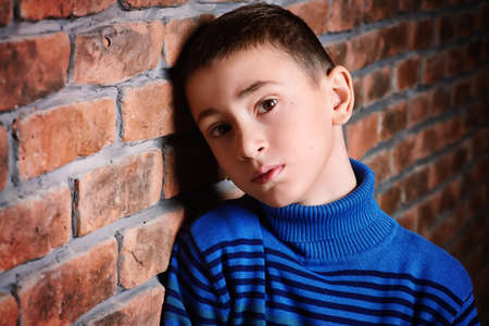 Portrait of a sad nine year old boy leaning against the brick wall. Clothes for children. Kid's fashion.の写真素材