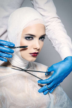 Beauty, fashion and medicine, plastic surgery. Portrait of an attractive young woman in bandages and hospital gown. Studio shot.の写真素材