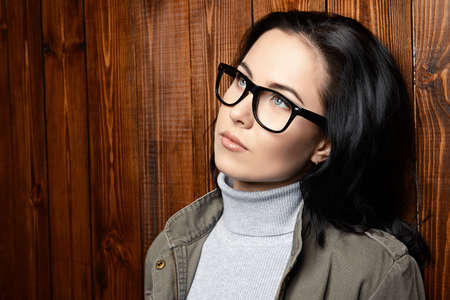 Young woman in glasses standing by the wooden wall. Business casual style. Optics.の写真素材