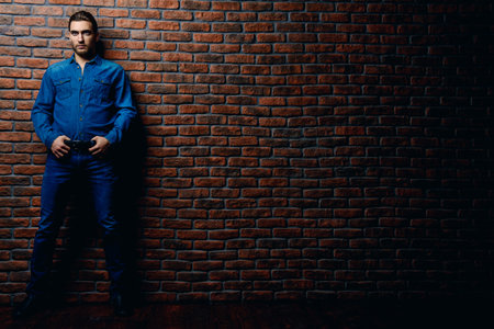 Jeans style. Full length portrait of a handsome young man in jeans clohes standing against the brick...