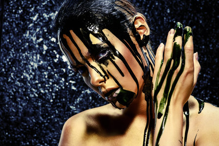 Beauty provocation. Body painting project. Portrait of a young woman with golden skin and black oil...