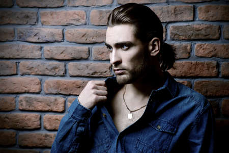 Jeans style. Portrait of a handsome young man in jeans clohes standing against the brick wall. Men's beauty, fashion. Men's barbershop, Hairstyle.の写真素材