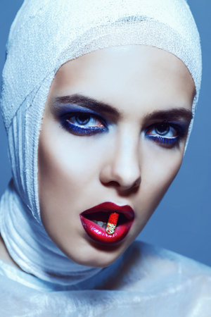 Close-up portrait of an attractive young woman in bandages holding a pill capsule in her mouth....
